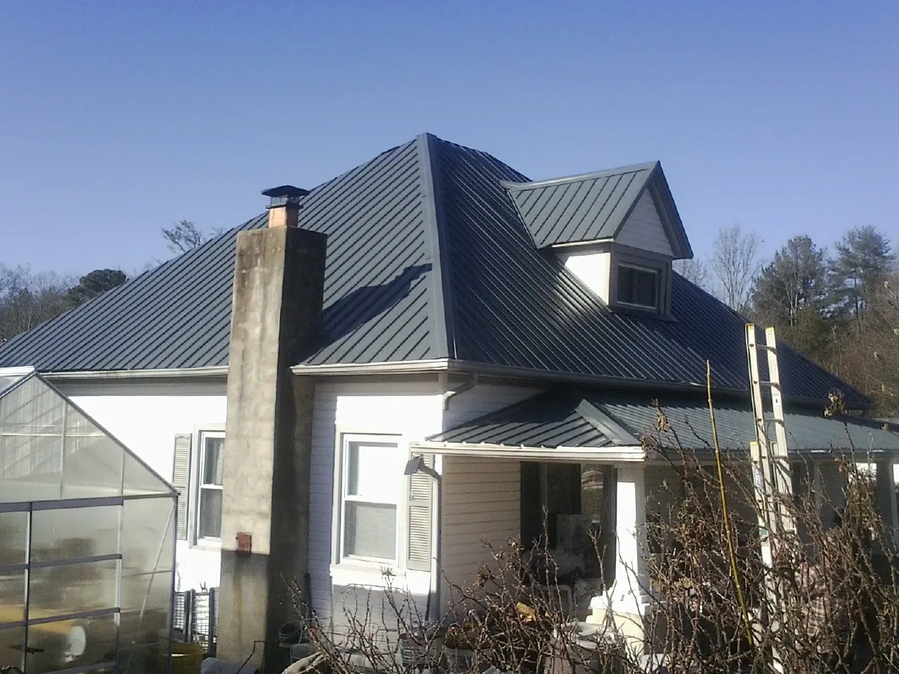Dark blue standing seam metal roof on a white farmhouse with dormer — Slate & Tile Roof Repair by Roofing Brothers in Paynes Creek