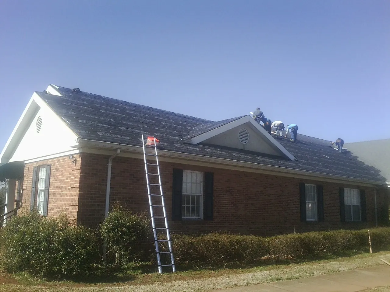 Crew tearing shingles off a brick ranch roof with a ladder set — Metal Roof Repair work by our crew in Paynes Creek