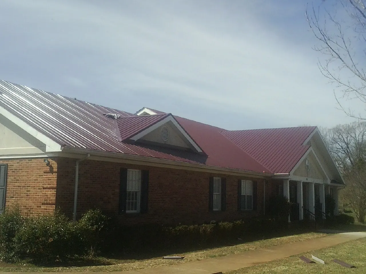 Red metal roof with gabled entries on a long brick building, from a Hail Damage Roof Repair job in Paynes Creek