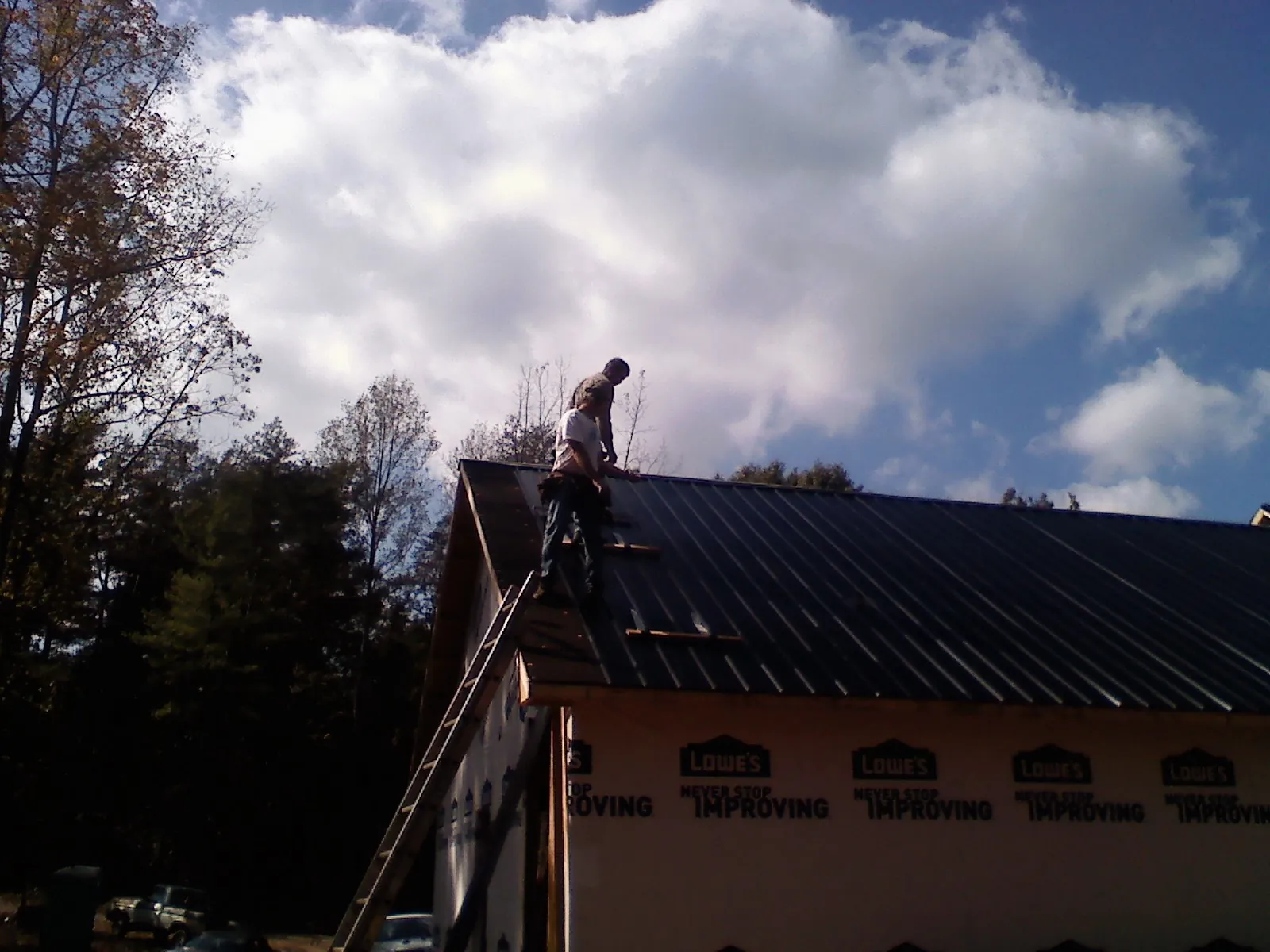 Roofer fastening dark metal panels high against a cloudy sky, from a Roof Inspection job in Paynes Creek