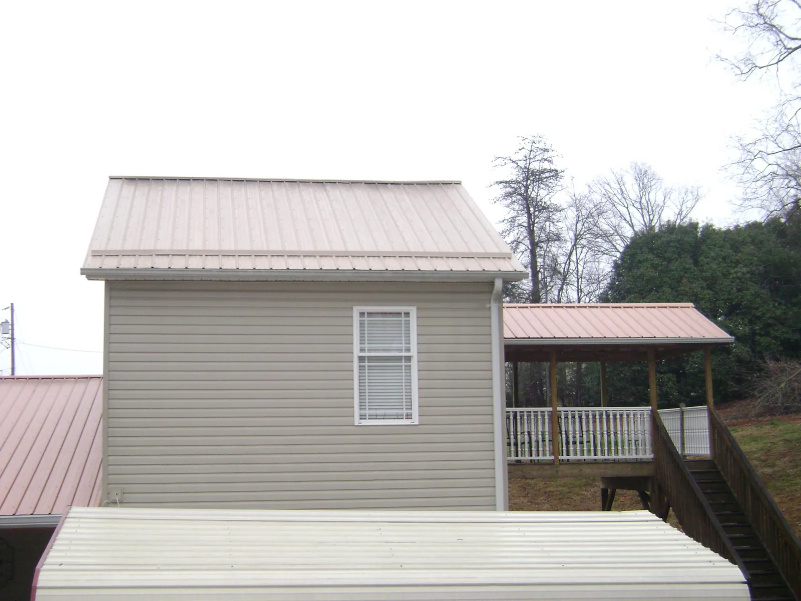 Tan metal roofs on a two story addition and attached porch, from a Roof Replacement job in Paynes Creek